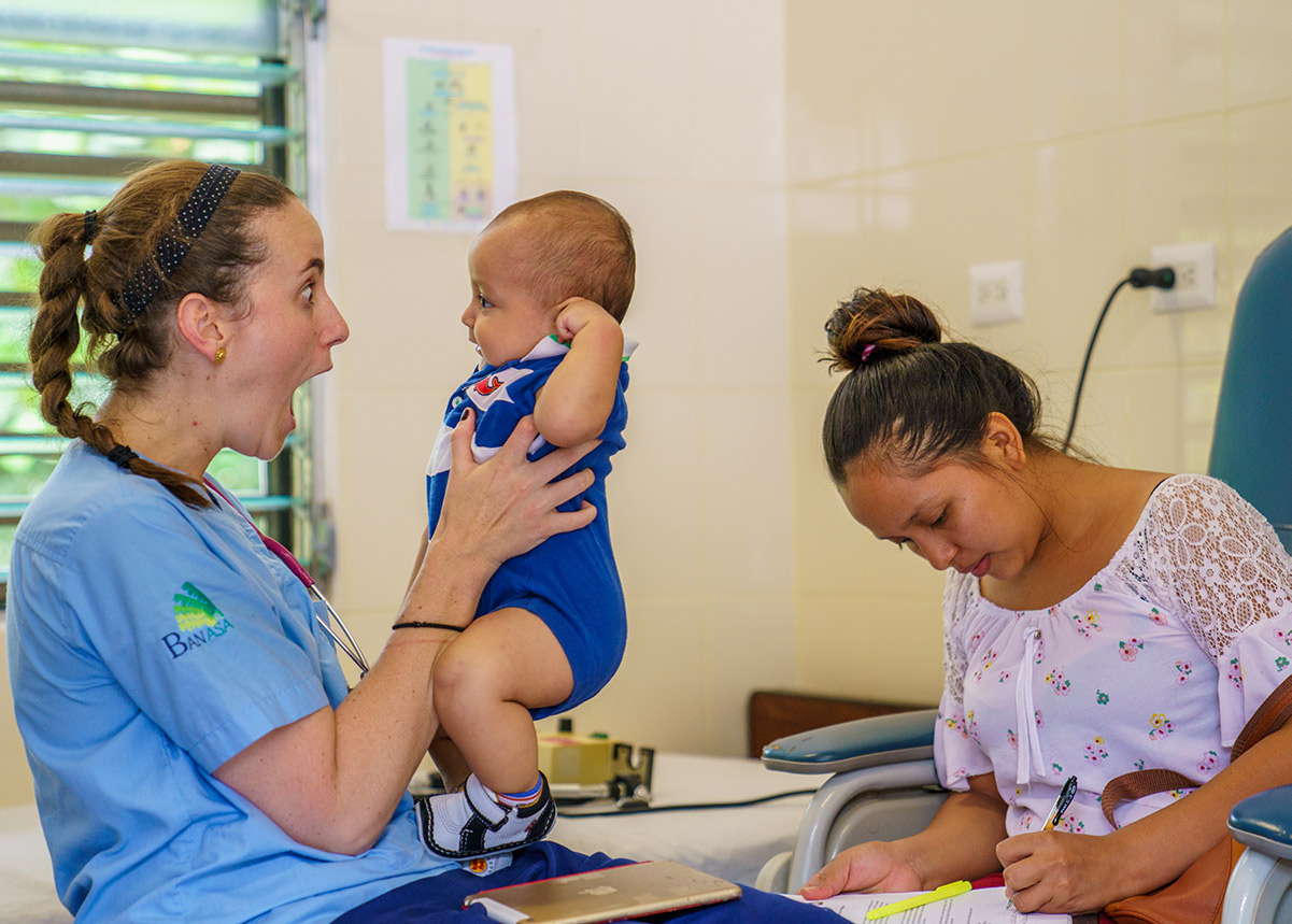 nurse holding a baby and a woman filling out paperwork in the background