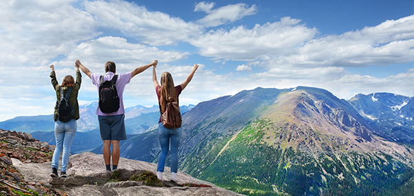 group of hikers on top of mountain looking at view with hands raised