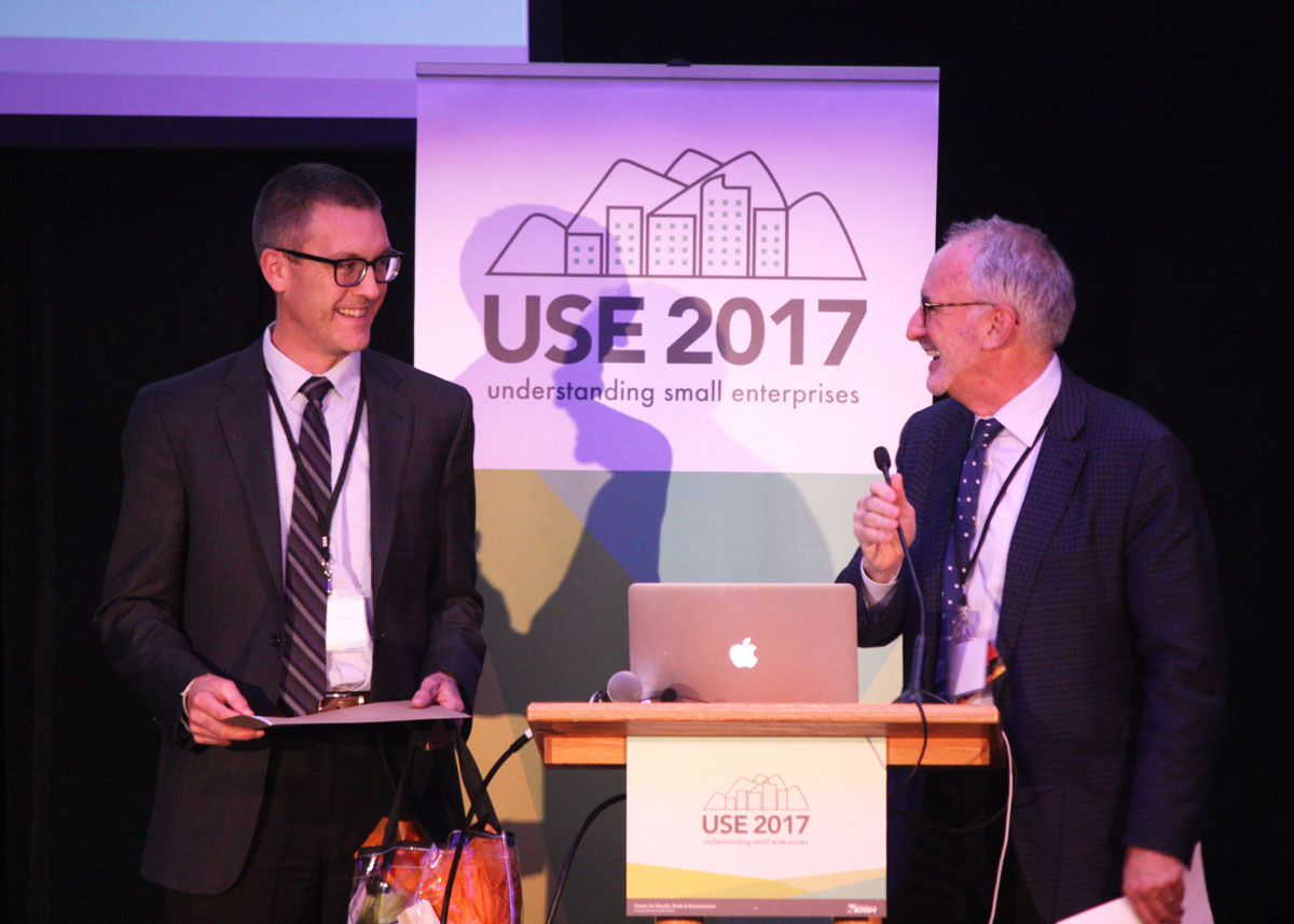 Lee Newman and Tom Cunningham on stage standing in front of a USE Conference banner