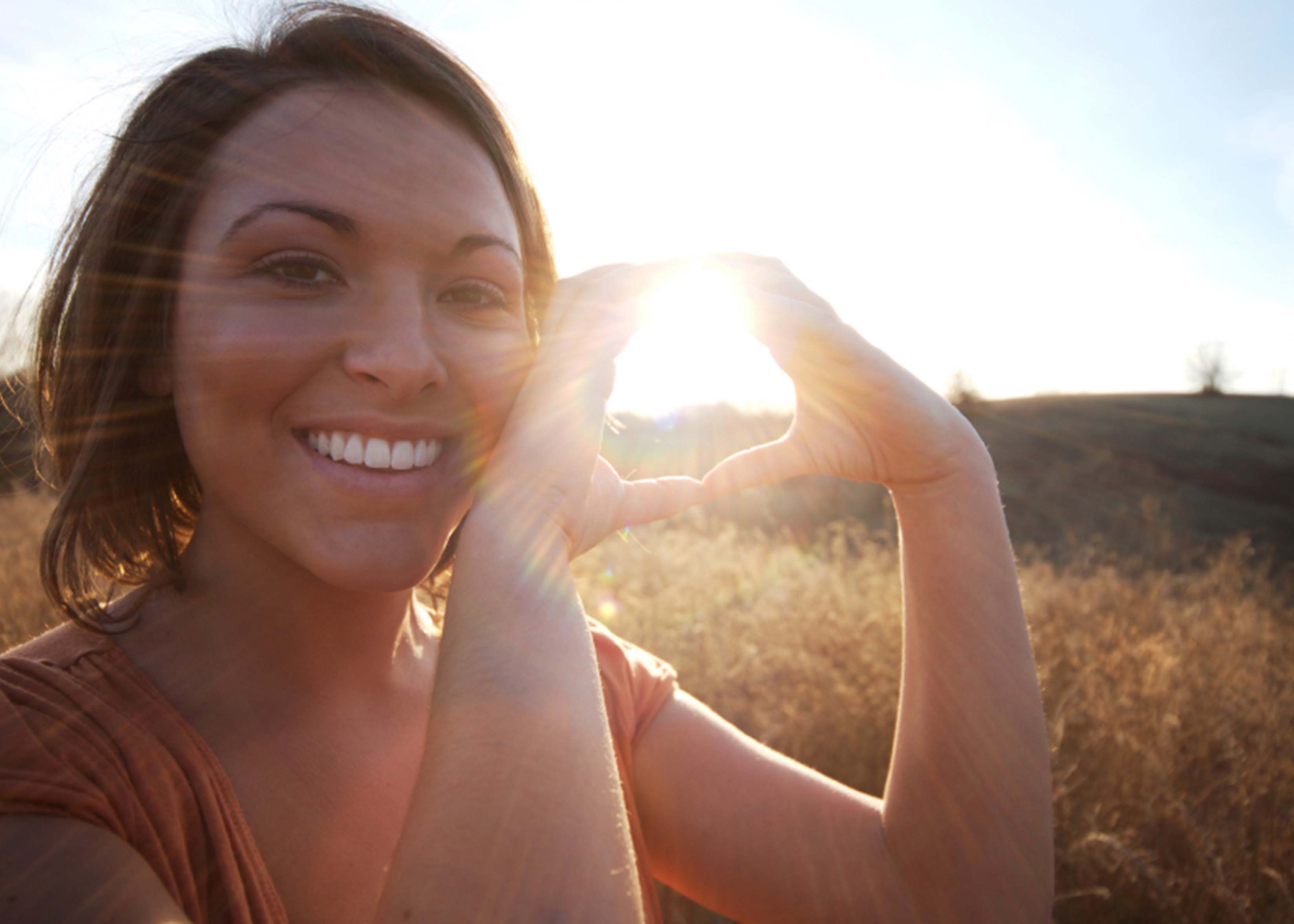 Young Native woman making a heart symbol with her hands in front of a sunset