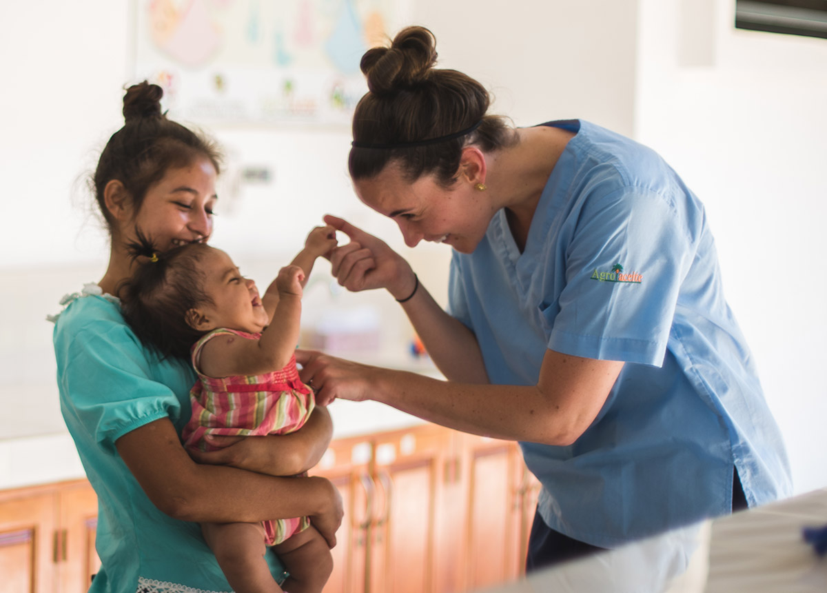 healthcare worker playing with child who is being held by a woman