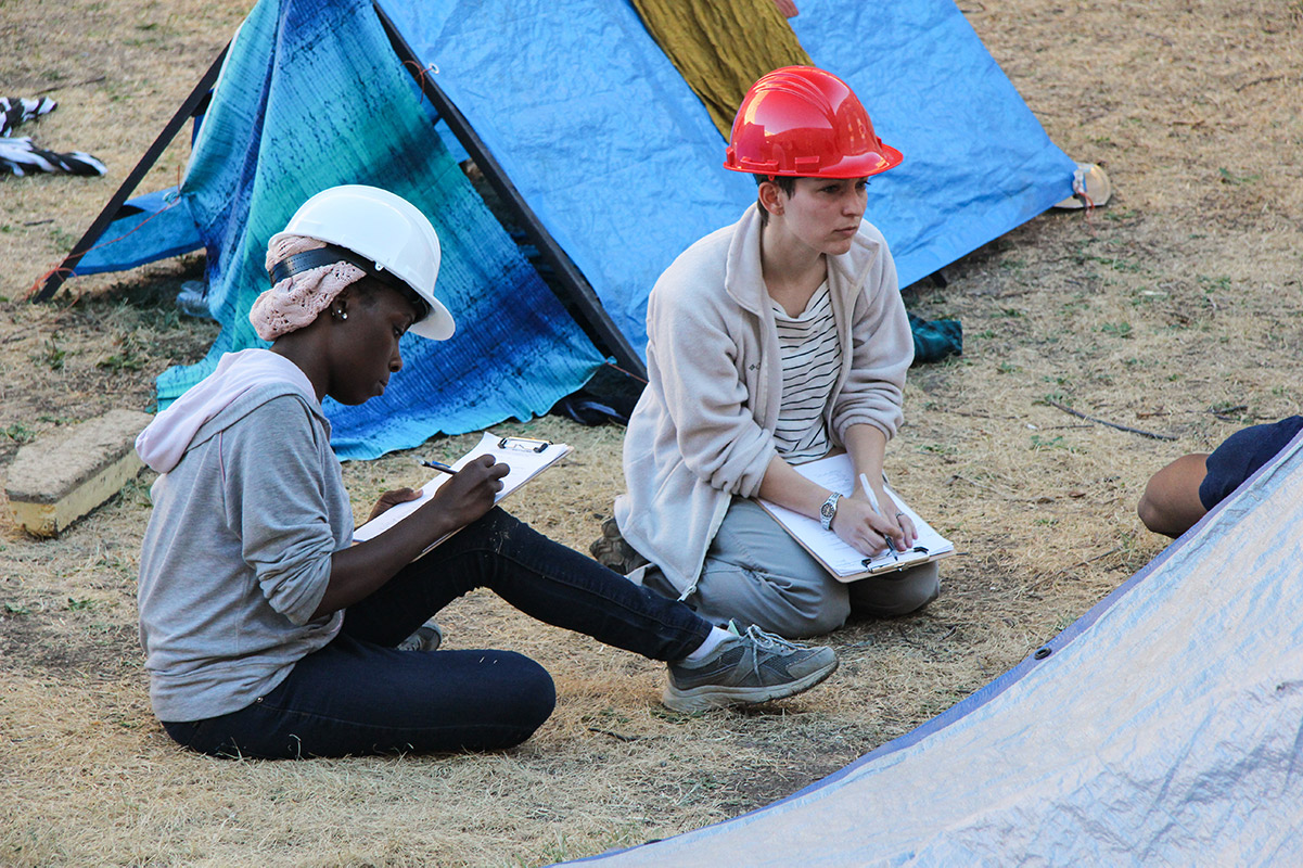 two students in hard hats taking notes at a disaster prepardness drill