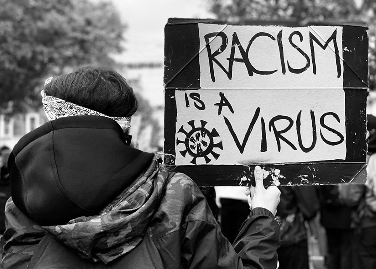 protester holding a sign that reads "racism is a virus"