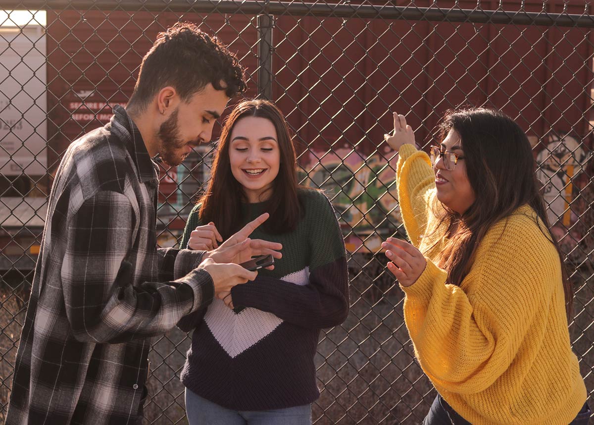 three teenagers talking against a fence