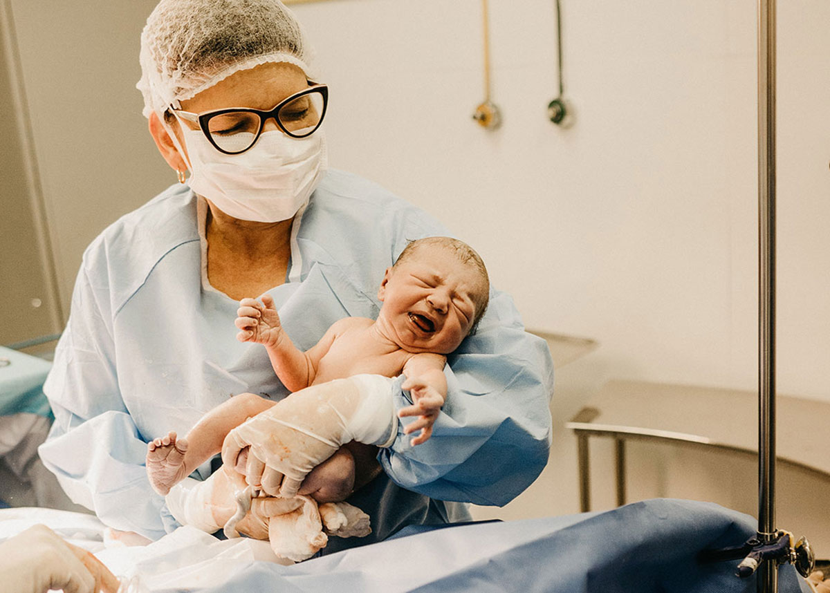 woman wearing a surgical mask holding a newborn baby