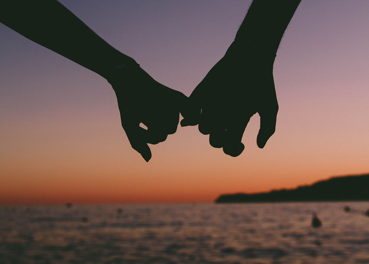 two hands holding each other with a sunset in the background