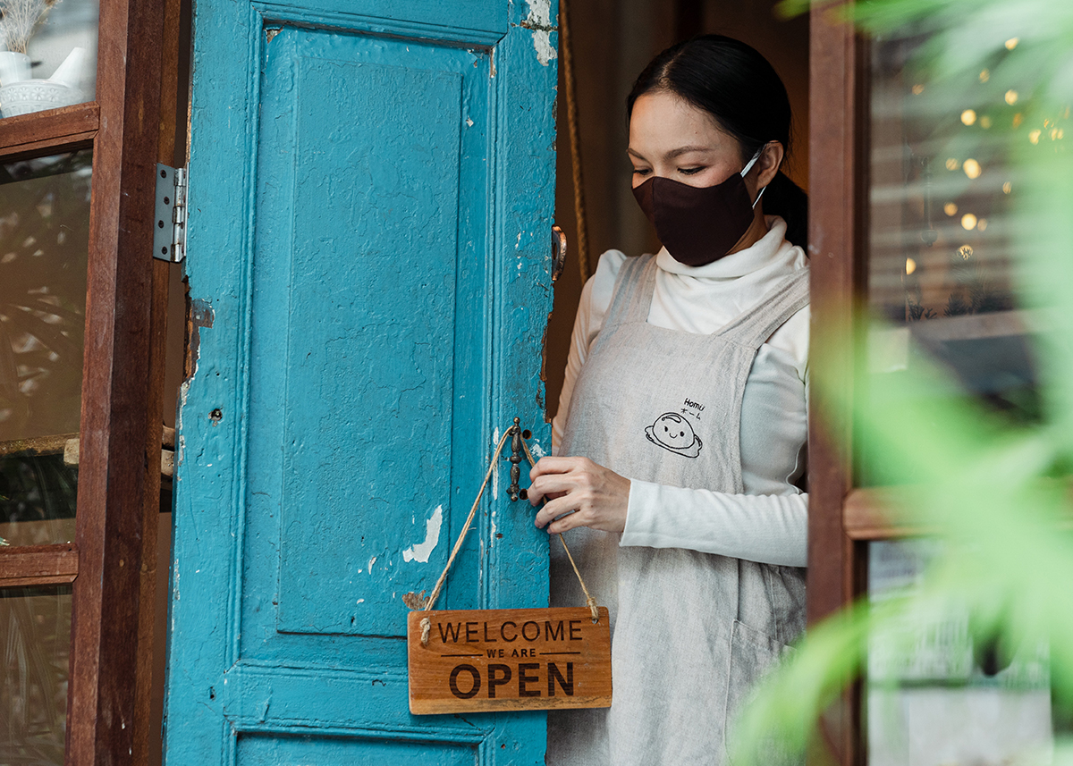 woman wearing face mask hanging open sign on business door