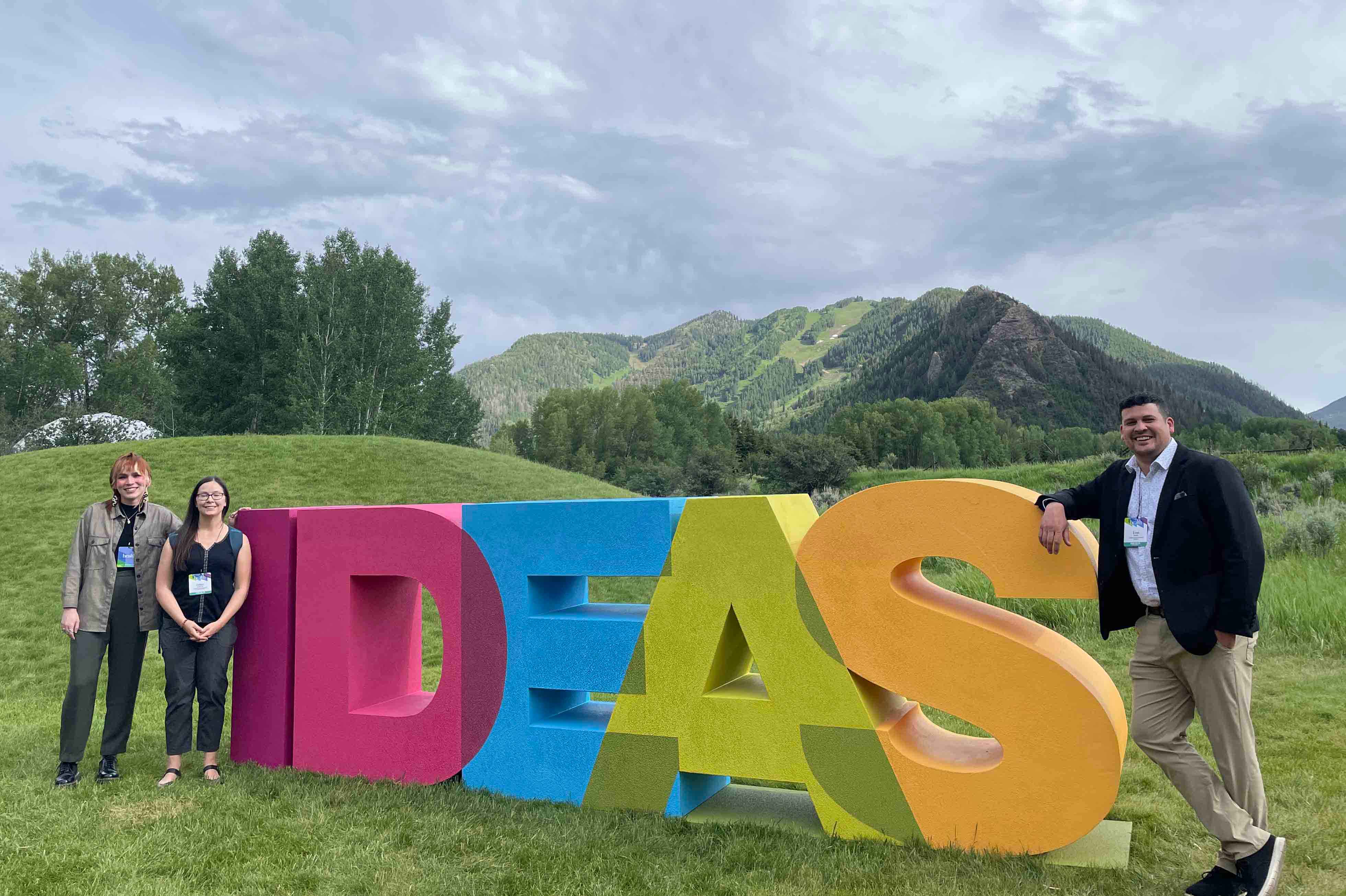 Evan, Helen, and Cass pose in front of big block letters that spell 