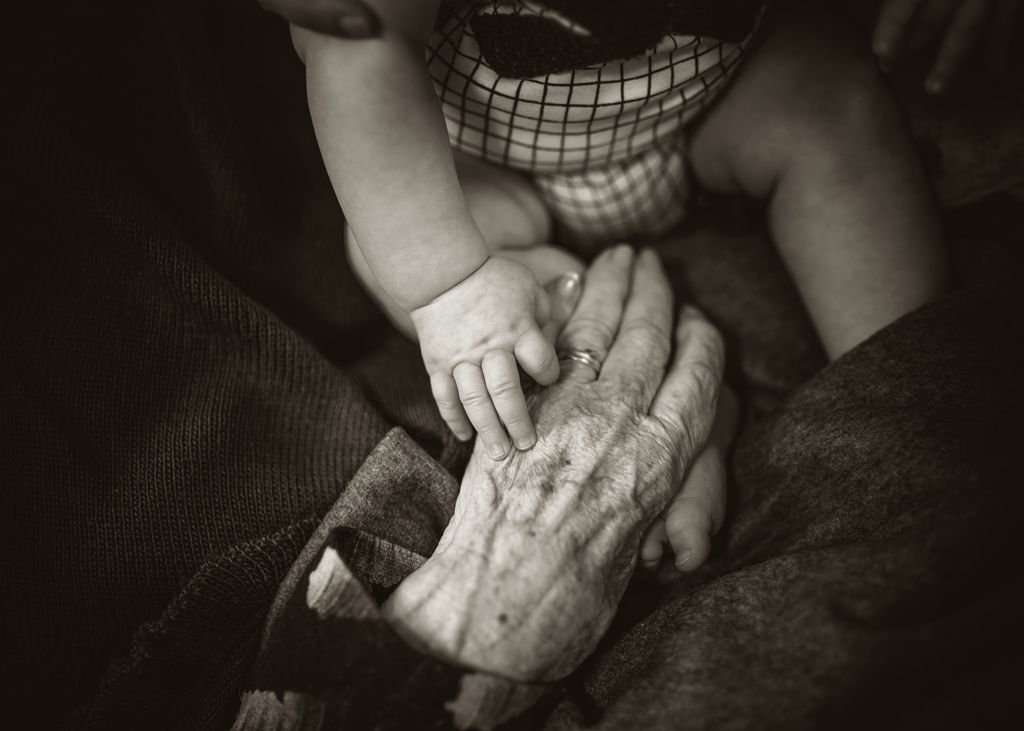An elderly person holding a babies hand