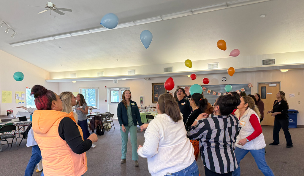 A group in a circle trying to keep multiple balloons up in the air