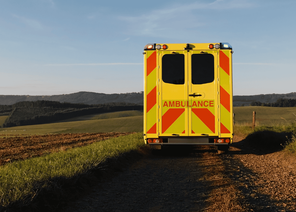 Ambulance during daytime driving through a very rural location with a single, dirt road