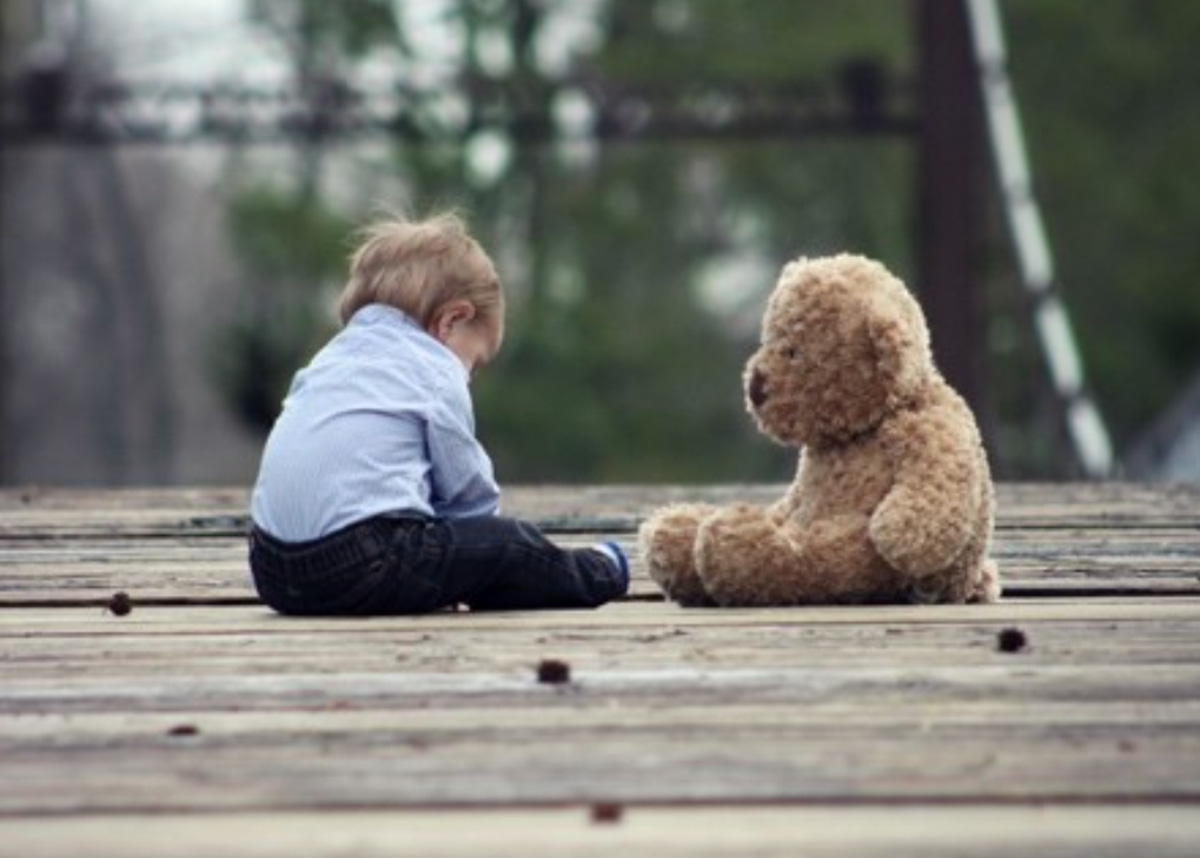 Glum child sitting on outside across from a teddy bear
