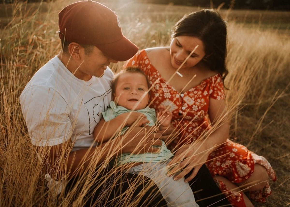 family of two adults and a baby smiling in a field