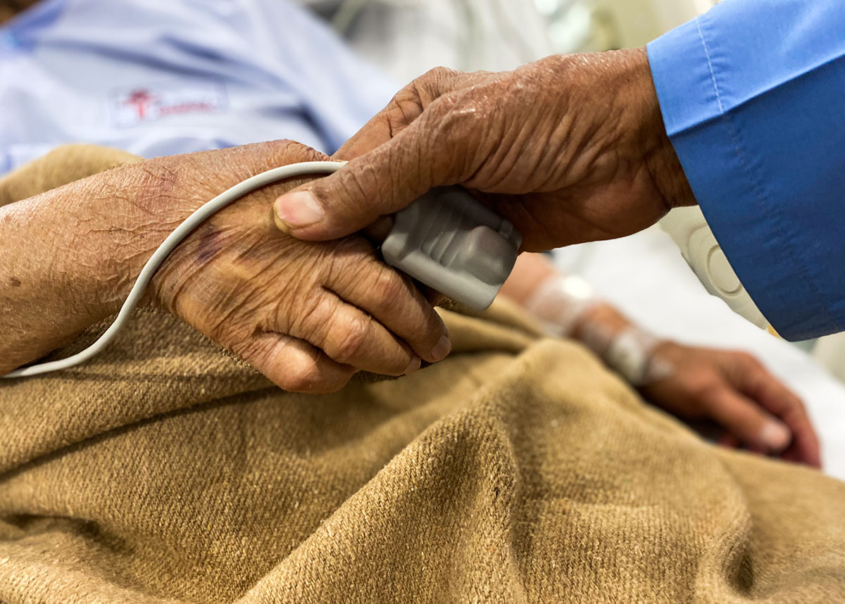 Close up of a person holding an older adults hand in a hospital bed