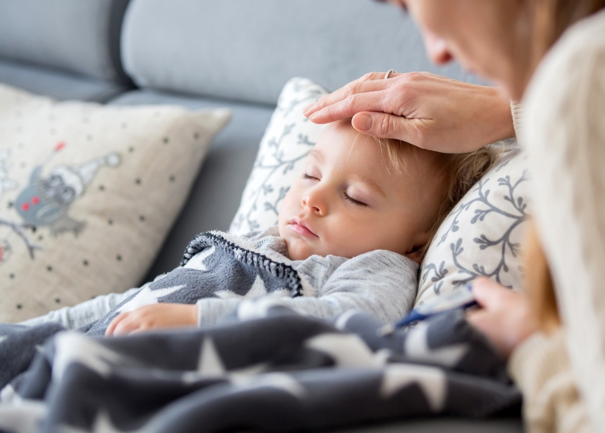 Sick child, toddler boy lying in bed with a fever, resting at home