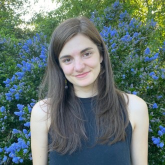 Headshot of woman wearing navy top in front of blue flowers