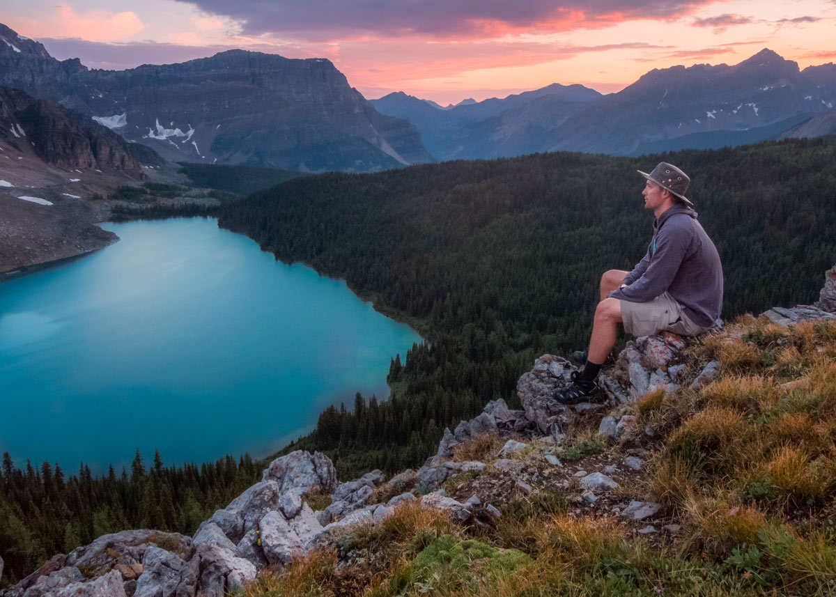 man sitting on a rock in nature looking out on mountains and a lake