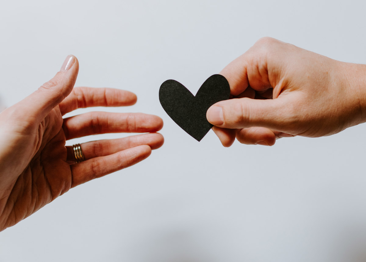 hands handing over a small paper black heart