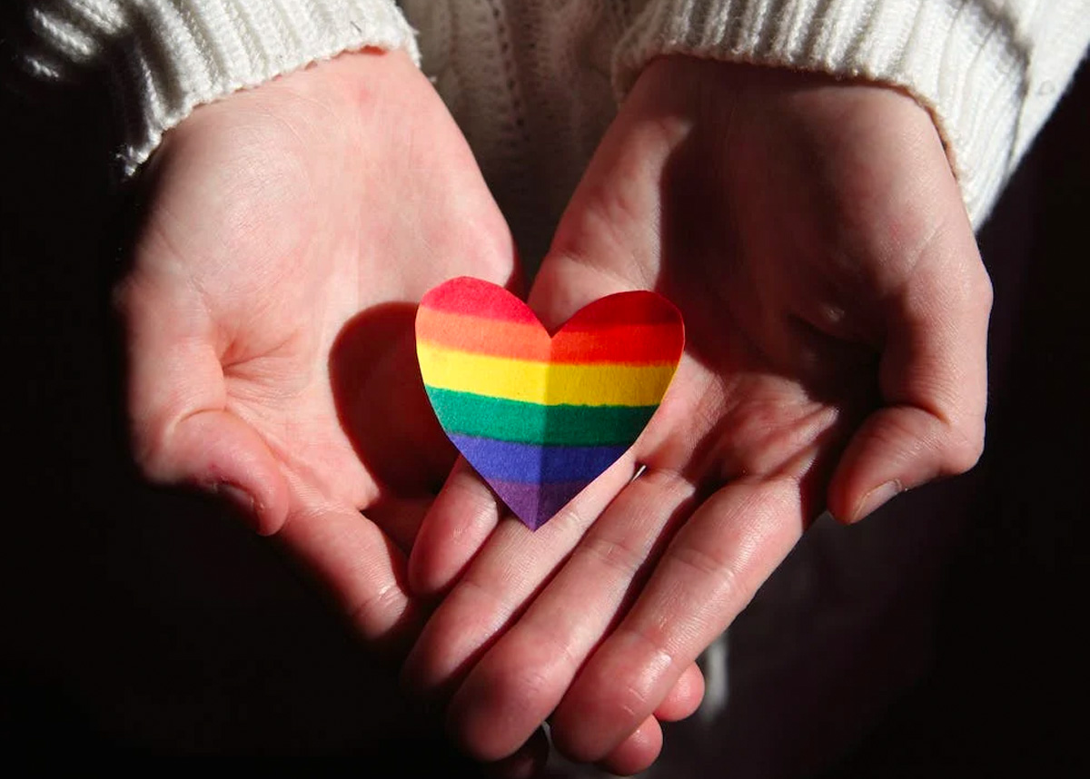 Person holding paper heart in hands with rainbow stripes