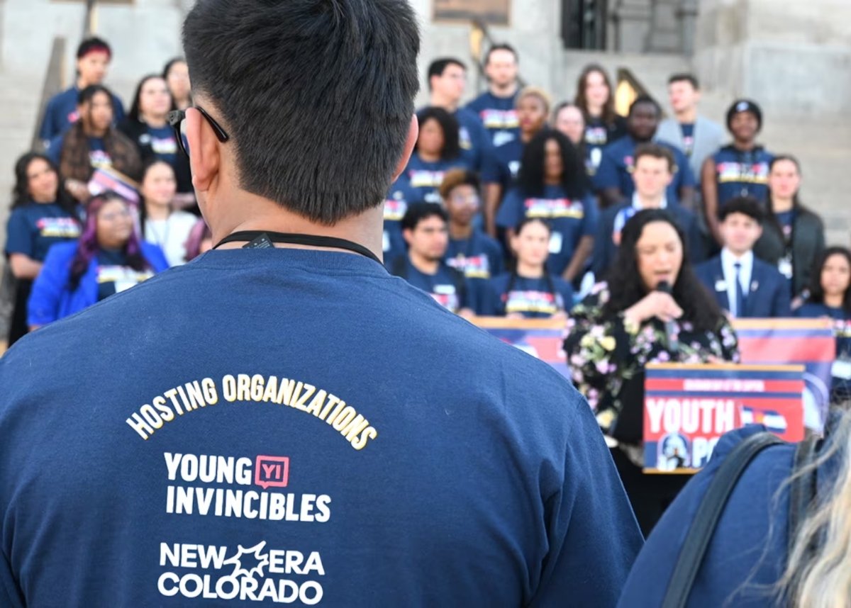 Crowd with speaker, focus on a man's back, shirt of New Era Colorado