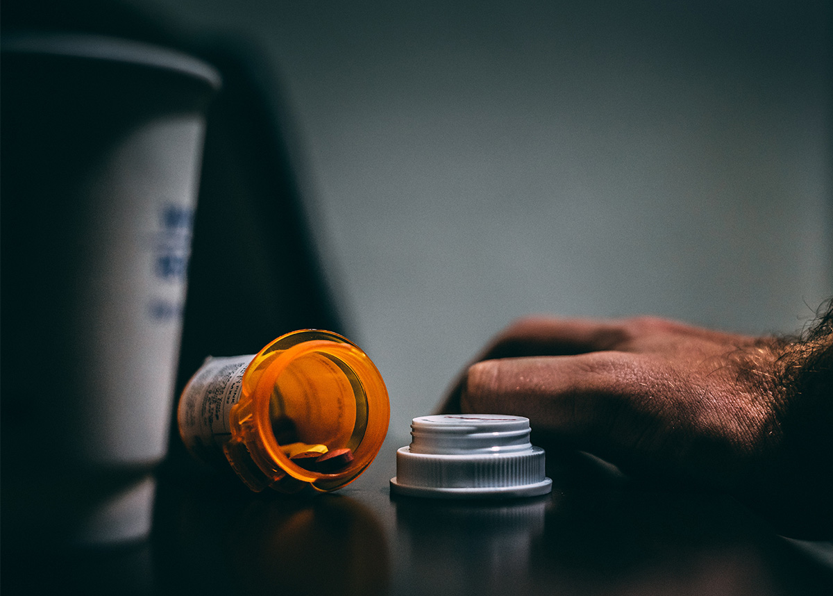 close up of persons hand next to pill bottle on table
