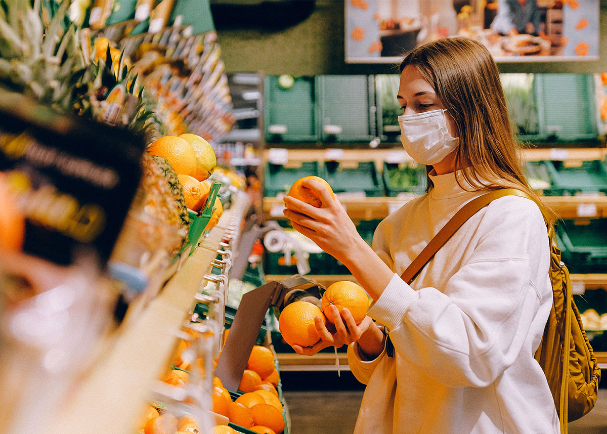Person wearing a mask at grocery store, holding an orange at fruit stand