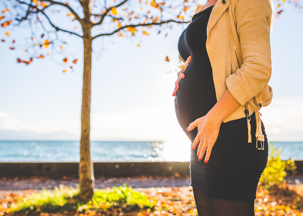 Close up of pregnant person outdoors, with their hands on their stomach