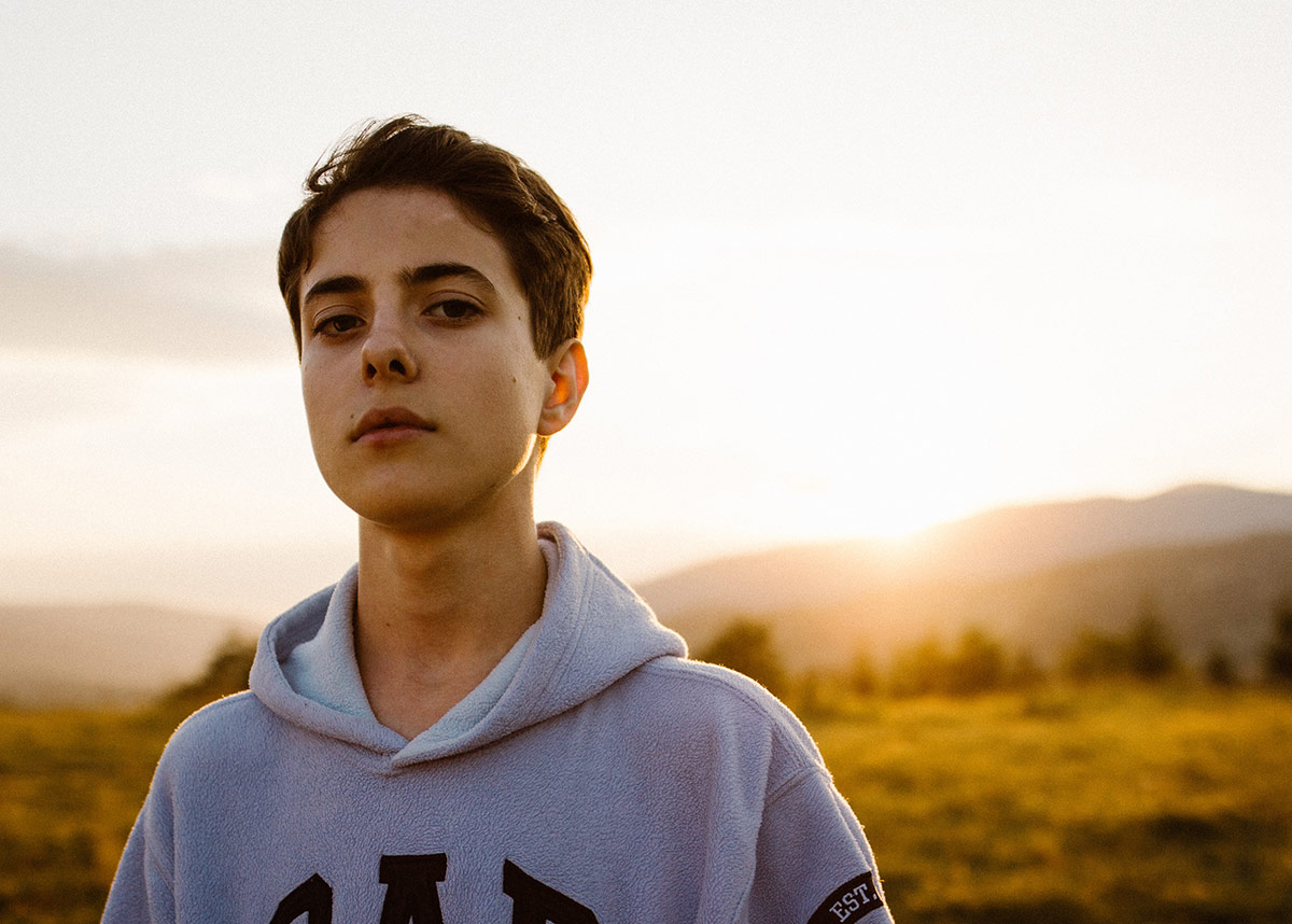 young man in gray sweatshirt in a field at sunset