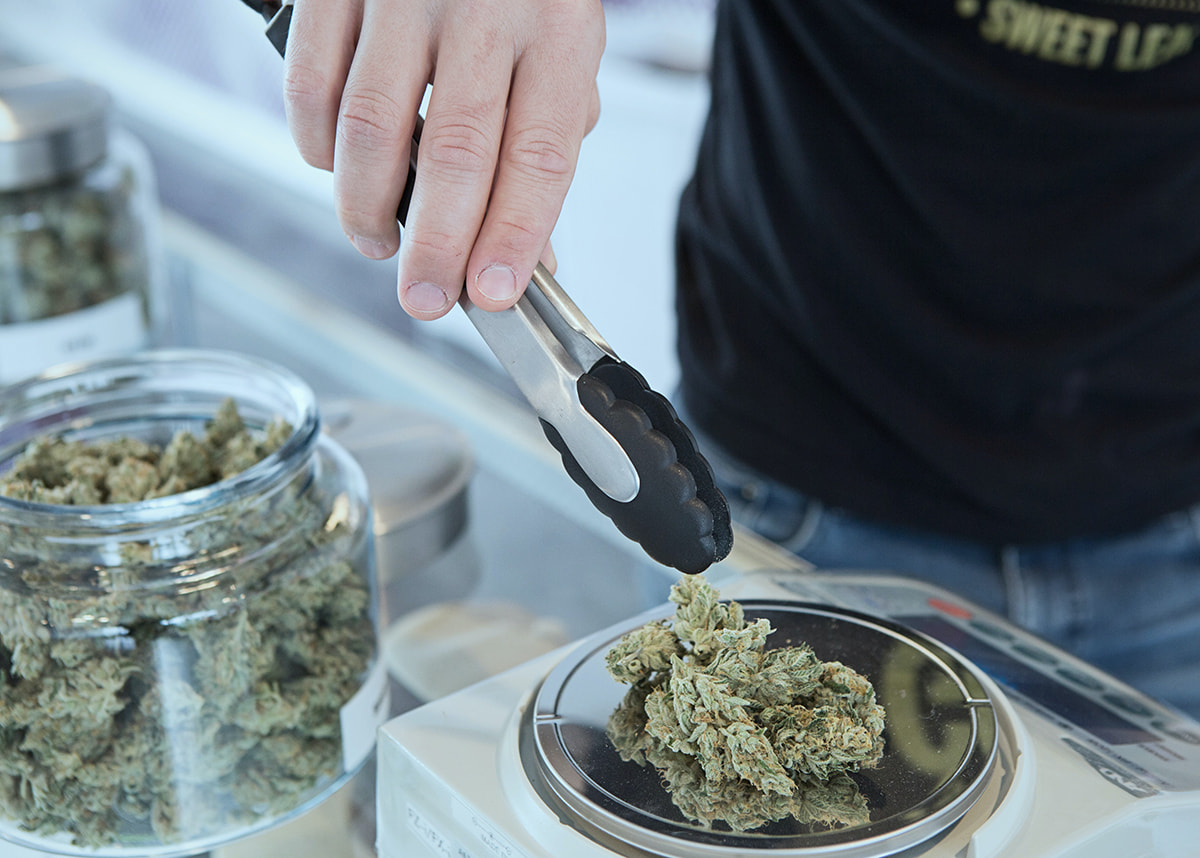 Close up of hand with tongs weighing marijuana products on a scale