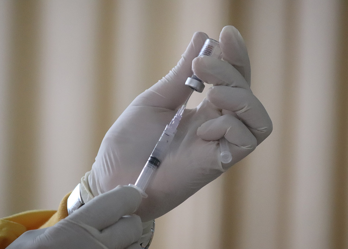 gloved hands pulling vaccine out of a vial into a syringe