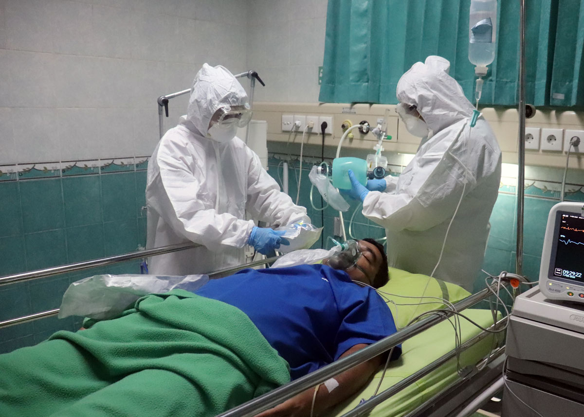 two healthcare workers in full ppe at the bedside of a patient in a hospital