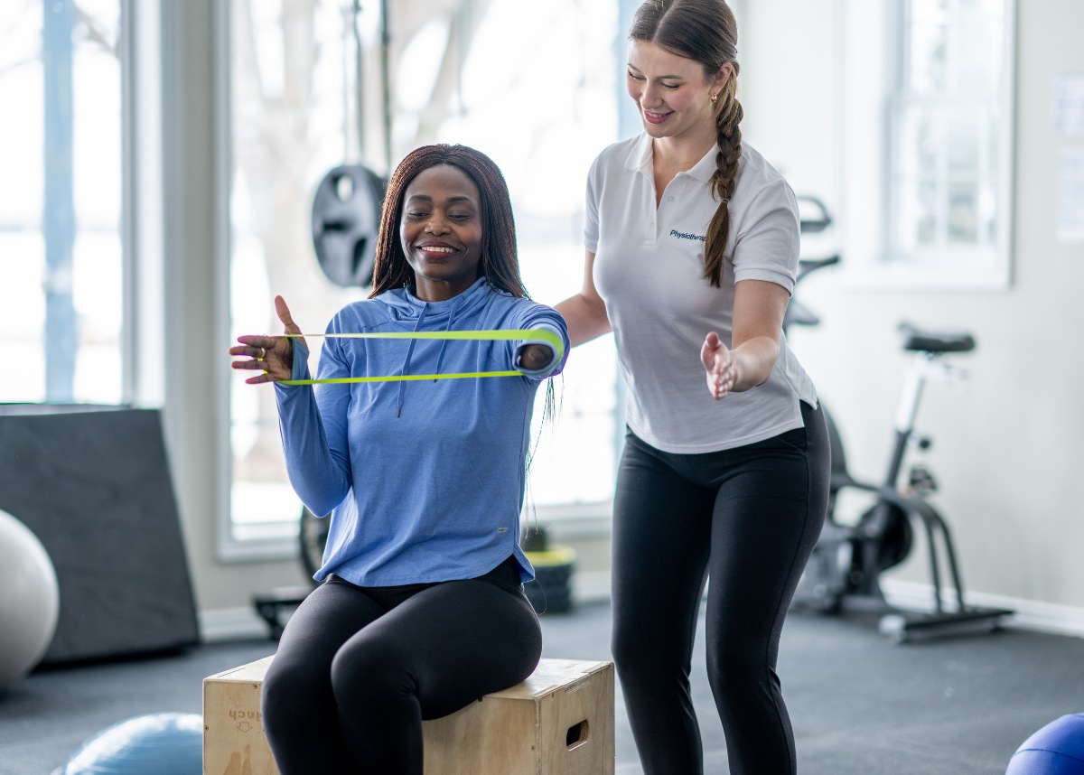 Woman helping patient using resistance band on her arms