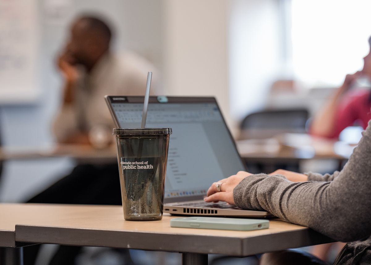 student typing on laptop with cosph cup in front