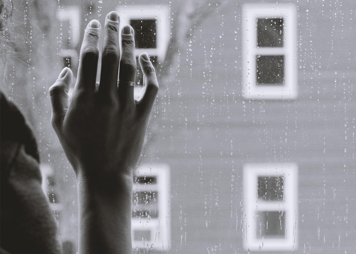 Black and white image, close up of hand on rainy window