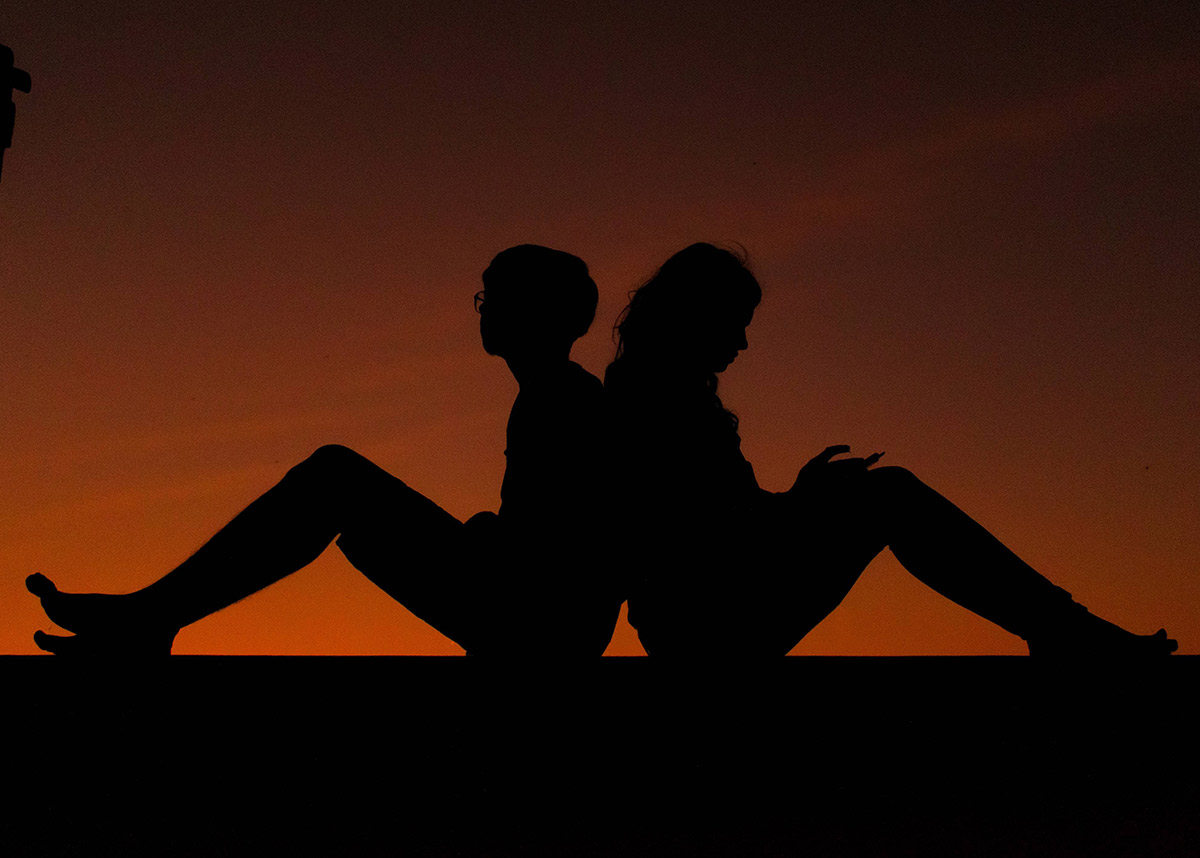 silhouette of two young people sitting back to back