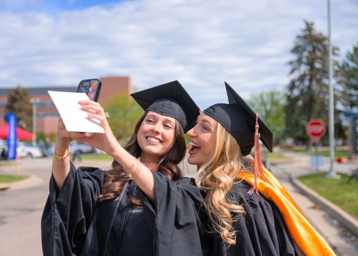 two women in college graduate gowns taking a selfie