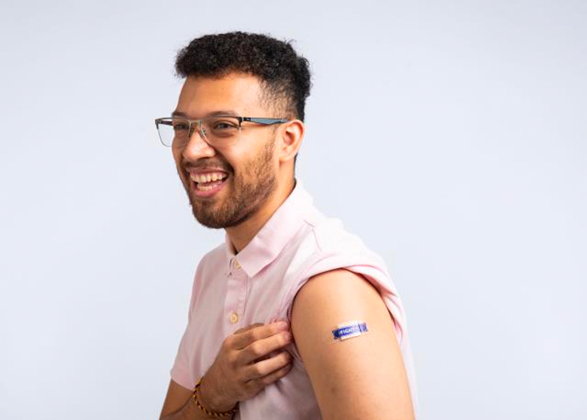 Person holding up sleeve, smiling and showing bandaid from vaccination