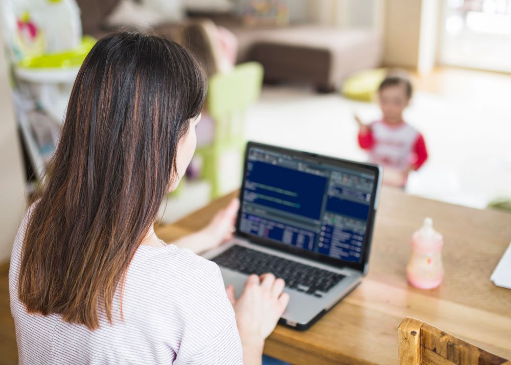 woman typing on laptop with child in background