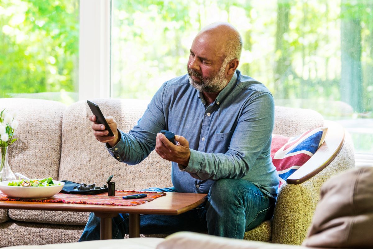 Mature diabetic man testing his blood sugar and using a smartphone