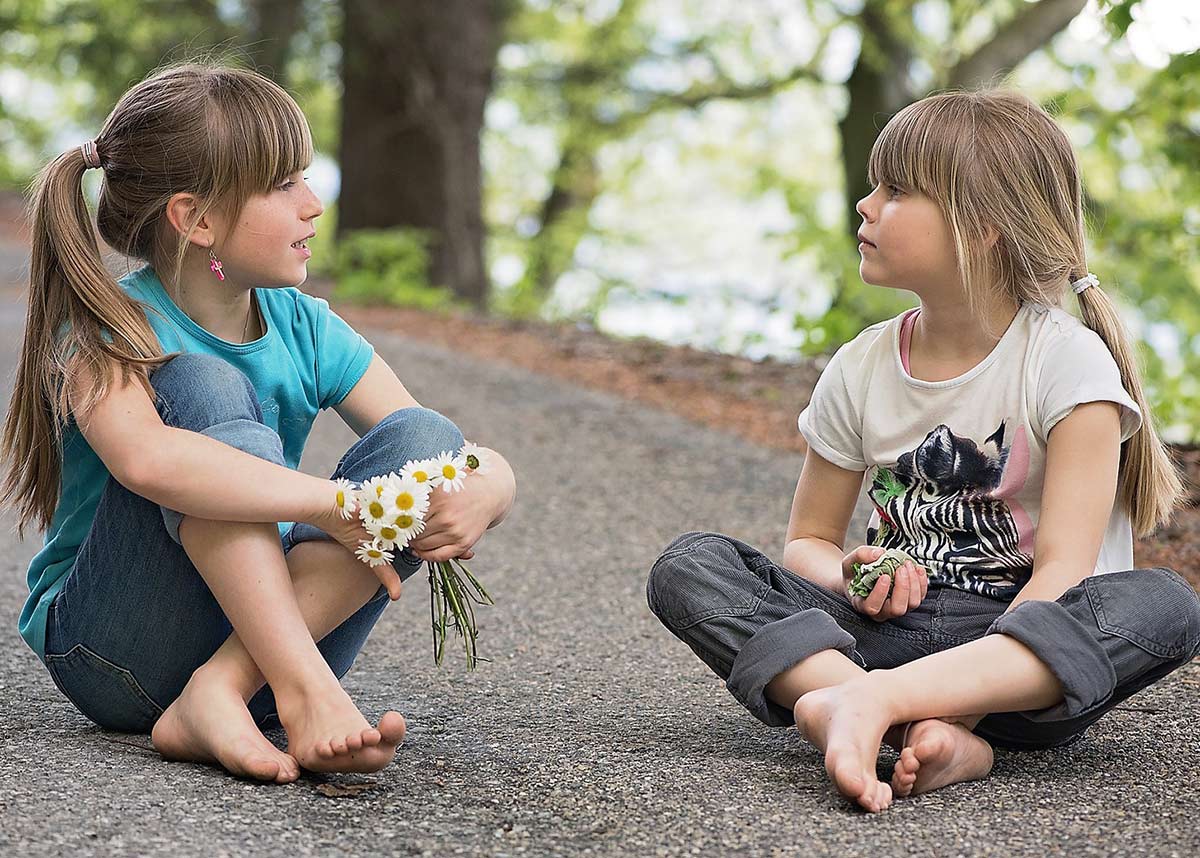 two young girls sitting on pavement and talking